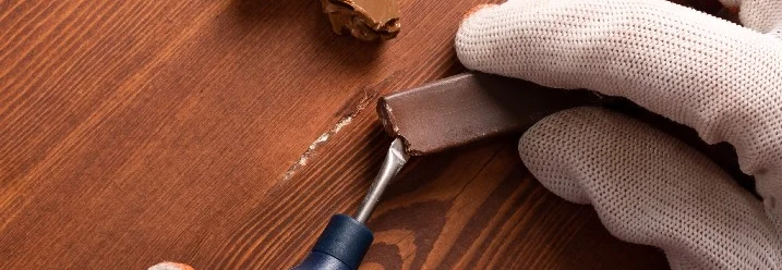 Person repariert Kratzer im Holz